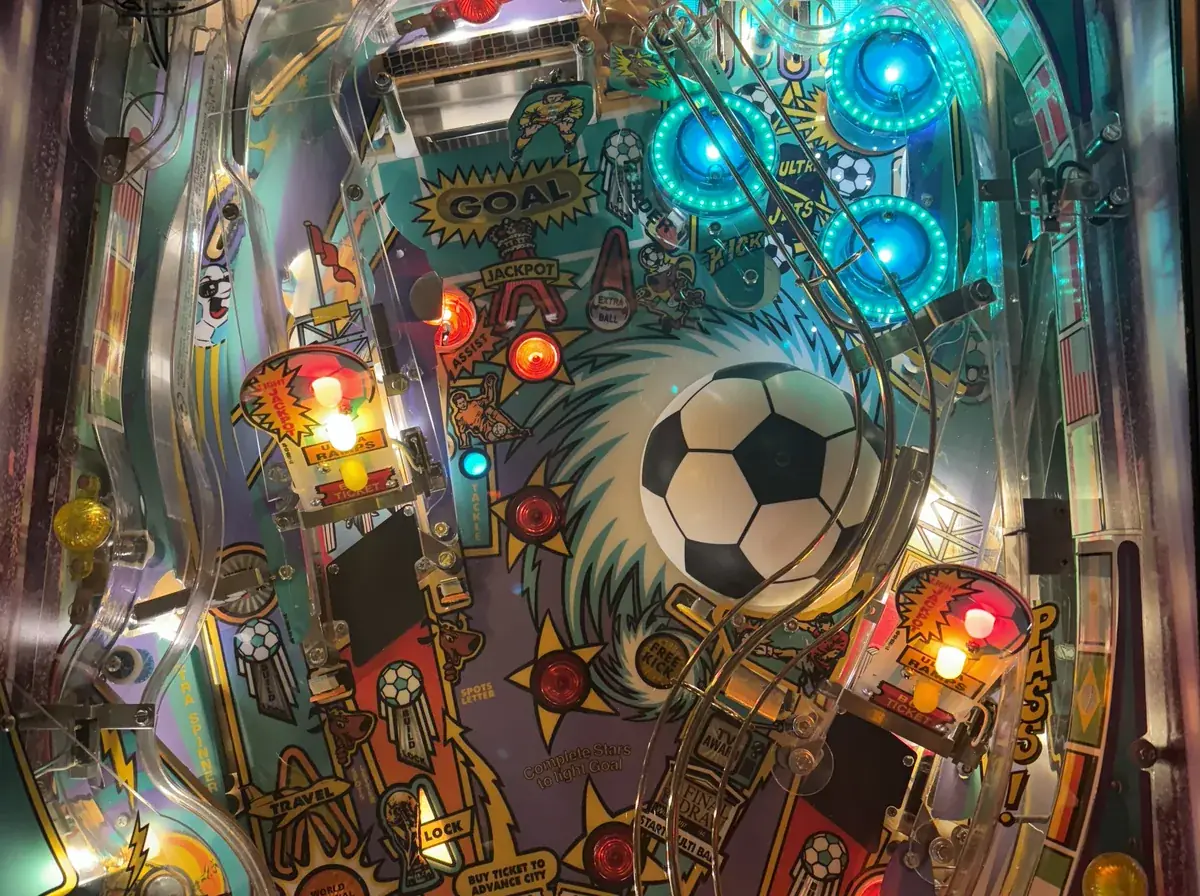Opened pinball playfield under a bench lamp mid-restoration